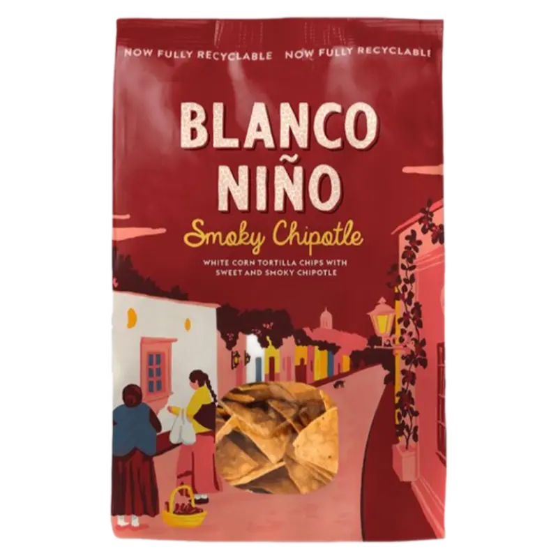 A bag of Blanco Niño Smoky Chipotle white corn tortilla chips, featuring a dark red packaging design with an illustrated street scene and a clear window showing the chips inside.