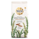 A 500g bag of Biona Organic Spelt Fusilli Wholegrain pasta on a solid white background. The packaging is off-white with a gold circular logo, green and olive botanical illustrations, and brown pasta pieces shown in the center.